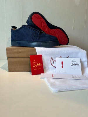 Christian Louboutin skor - Snygga mörkblå sneakers i mocka från Christian Louboutin med den ikoniska röda sulan. Klassisk låg modell med matchande mörkblå snörning och diskreta sömmar. Perfekta för dig som vill ha en exklusiv och stilren look.