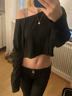 Svart croppad offshoulder topp - Säljer en svart croppad topp med offshoulder-design och långa ärmar. Toppen har en loose passform och är perfekt för dig som gillar en avslappnad men ändå trendig stil. Passar till både jeans och kjol för en cool look.