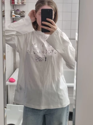 Vit långärmad t-shirt med tryck från Acne Studios med glitter - Säljer en vit långärmad t-shirt med silvrigt tryck framtill. Tröjan har en loose passform och är tillverkad i mjuk bomull. Perfekt för en avslappnad och chill stil. Acne studios. 15% hampa 85% bomull.