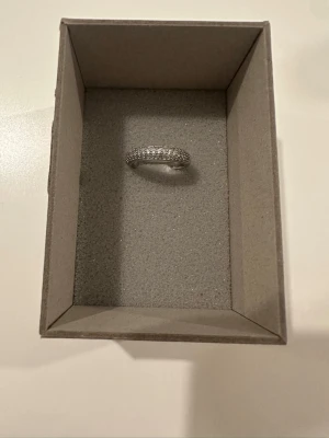 Silverfärgad ring med gnistrande stenar - Stilren silverfärgad ring med flera rader små gnistrande stenar runt hela bandet. Ringen har en klassisk, rund form och ger ett elegant intryck. Perfekt för dig som gillar smycken som sticker ut lite extra.