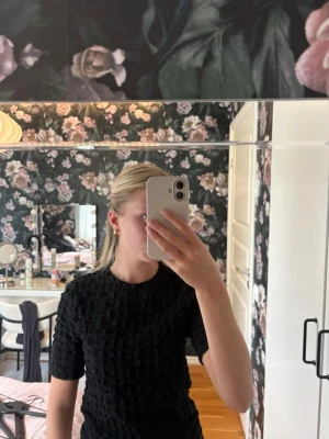 Svart ribbad topp med struktur - Säljer en svart topp med ribbad struktur och korta ärmar. Toppen har en rund halsringning och är tillverkad i ett stretchigt material som sitter snyggt på kroppen. Perfekt att styla med både jeans och kjol🌸