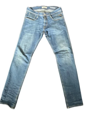 Blåa replay anbass - Snygga blåa jeans från Replay i slim fit-modell med klassiska fickor och diskreta slitningar. Jeansen har raka ben och kontrastsömmar, samt Replay-logga på bakfickan. Perfekta för en avslappnad och trendig look. Modell: Anbass. Storlek: 30/32 Nypris: 1300kr.  Mitt pris:499kr.