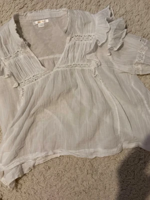 Vit blus med volanger från Gina Tricot 14+ avdelning från Ullared  - Söt vit blus från Gina Tricot med volangdetaljer och spetsinslag. Blusen är gjord i ett tunt, luftigt tyg som ger en romantisk känsla, lite genomskinlig men med ett vitt linne under passar det perfekt. Perfekt för en trendig och avslappnad look. Använt 2 gånger 
