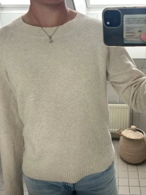 Beige stickad tröja med rund hals - Mysig beige stickad tröja med rund halsringning och långa ärmar. Tröjan har ribbstickade muddar vid ärmslut och nederkant. Perfekt för lager på lager och enkel att matcha med jeans eller kjol. Har använts många gånger och har blivit lite tussig. 