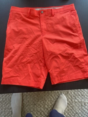 Röda shorts från Callaway - Röda shorts från Callaway i storlek EU 48. Tillverkade i en mix av 65% polyester och 35% viskos. Klassisk modell med bälteshällor och fickor, perfekta för sportiga aktiviteter under sommaren.  