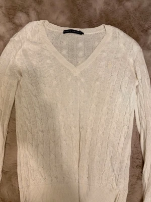 Vit  tröja Ralph Lauren - Kabelstickad vit tröja från Ralph Lauren med V-ringning och långa ärmar. Klassisk design med ribbade muddar och mjukt material som passar perfekt till många olika stilar. Enkel att matcha och riktigt snygg till jeans eller kjol.