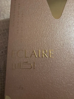 Eclaire Misi parfym - Lyxig parfym i en elegant, skimrande rosa förpackning med gulddetaljer. Förpackningen har en modern och stilren design med präglad text. Perfekt för dig som vill ha en exklusiv doftupplevelse.