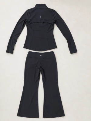 Svart loungewear set med utsvängda byxor - Snyggt svart loungewear set med figurnära zip-jacka och utsvängda byxor. Jackan har hög krage, långa ärmar och dragkedja framtill samt fickor med dragkedja. Materialet är stretchigt och mjukt, perfekt för chill dagar hemma.
