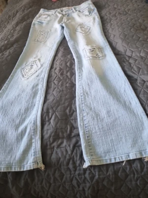 Ljusblå jeans med slitningar - Säljer ett par ljusblå jeans från Auposen med slitna fina detaljer och råa kanter vid benslut. Jeansen har klassisk femficksmodell och är gjorda i denim. Perfekta för dig som gillar en avslappnad och trendig stil. I storlek m. Jeansens  helhet är i väldigt fin skick bara jeansens nederkant är sliten bakifrån se sista bild