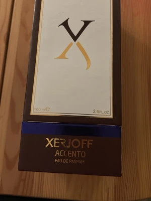 Xerjoff Accento Eau de Parfum 100ml - Lyxig parfym från Xerjoff, Accento Eau de Parfum i 100 ml flaska. Förpackningen är elegant i mörkbrunt och guld med inslag av blått. Använd en gång.