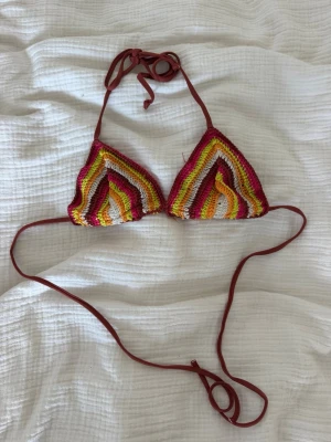 Flerfärgad virkad trekantsbikini - Snygg trekantsbikini i virkade ränder med färgerna vinröd, gul, orange, vit och rosa. Bikinin har knytband i vinrött och är perfekt för sommaren. Unik och färgglad stil som sticker ut på stranden. Sparsamt använd