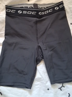 Svarta träningsshorts från SOC - Säljer ett par svarta träningsshorts från SOC med elastisk midja och logga runt linningen. Tillverkade i ett stretchigt och snabbtorkande material som passar perfekt för gym, löpning eller annan träning.
