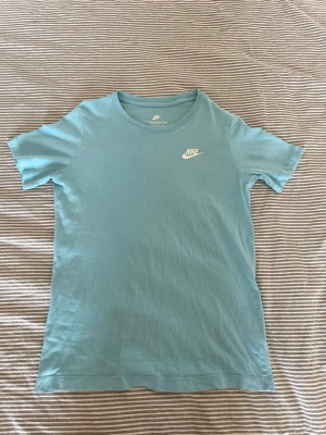 Ljusblå Nike t-shirt  - Snygg ljusblå t-shirt från Nike med klassisk logga tryckt i vitt på bröstet. T-shirten har rund halsringning och korta ärmar. Tillverkad i mjuk bomull för en skön känsla och enkel stil.
