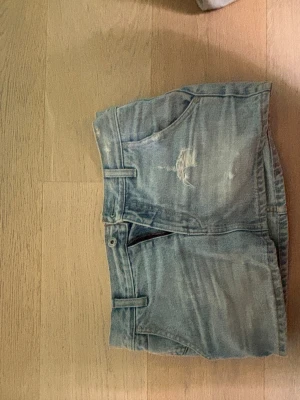 Ljusblå jeanskjol  - Säljer en ljusblå jeanskjol i kort modell med klassiska fickor både fram och bak. Kjolen har en avslappnad passform och slitna detaljer för en trendig look. Perfekt att matcha med en enkel topp eller hoodie. Midjemåttet är 38 cm ungefär och passar xs/s!