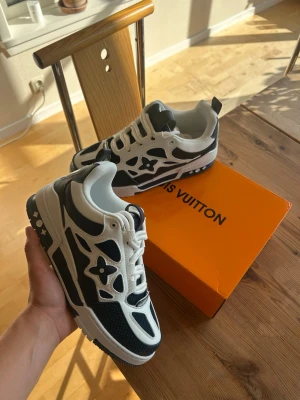 Louis Vuitton blåa och vita sneakers - Louis Vuitton sneakers i blått och vitt med ikoniska monogram-blommor på sidorna. Skorna har en chunky sula, meshpaneler och detaljer i läder. Snygg design med kontrasterande färger och tydliga LV-detaljer. Perfekta för dig som vill sticka ut med exklusiva sneakers.