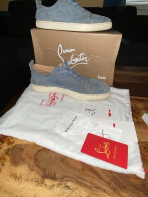 Blåa sneakers från Christian Louboutin - Snygga blåa sneakers i mocka från Christian Louboutin med vita sulor och matchande blå skosnören. Skorna har en låg profil och klassisk design med diskreta sömmar och beige innerfoder. Perfekta för dig som vill ha något exklusivt och stilrent.