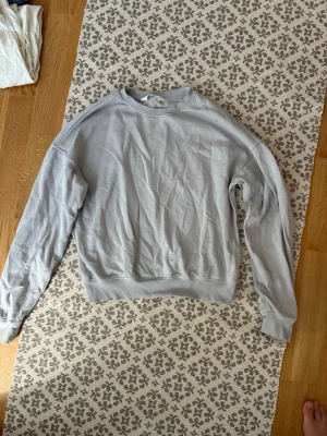 Ljusgrå basic sweatshirt - En enkel ljusgrå sweatshirt med rund hals och ribbade muddar vid ärmslut och nederkant. Tröjan har en avslappnad passform och är tillverkad i mjukt material, perfekt för en chill och stilren look. säljs pga att den inte använts tillräckligt mycket.