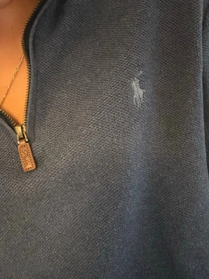 Mörkblå halvzip tröja från Polo Ralph Lauren - Mörkblå stickad tröja från Polo Ralph Lauren med halvzip och diskret broderad logga på bröstet. Tröjan har långa ärmar, ribbade muddar och en klassisk passform. Perfekt för lager på lager och enkel att matcha.
