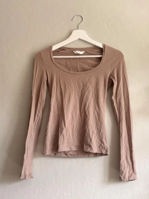 Beige långärmad topp - En enkel och stilren beige topp med lång ärm och rundad urringning. Tillverkad i mjukt material som känns skönt mot huden. Perfekt att matcha med jeans eller kjol för en clean look. Ny utan lapp men skrynklig…