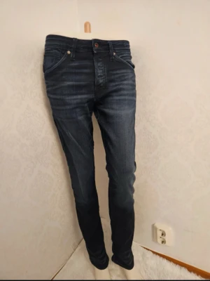 Mörkblå slim fit jeans - Säljer ett par mörkblå slim fit jeans med snygga slitningar och tvättade detaljer. Jeansen har fem fickor, normal midja och smala ben. Klassisk denimlook som passar till det mesta. Materialet är troligtvis bomull med lite stretch.