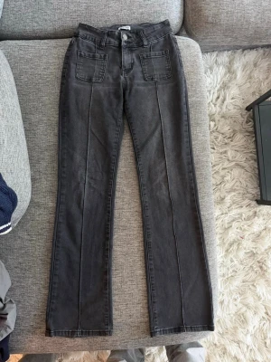 Svarta raka jeans MADLADY - Säljer ett par svarta jeans med raka ben och markerad pressveck framtill. Jeansen har två stora fickor fram och två bakfickor med lock och knapp. Klassisk femficksmodell i mjukt denimtyg, perfekta till vardagslooken.