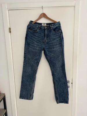 Blå raka jeans från Skagen - Snygga blå jeans från Skagen med klassisk rak passform och fem fickor. Jeansen har en vintage tvätt och tydliga kontrastsömmar. Perfekta för en avslappnad och trendig look. Saknar knappen för att knäppa byxorna men annars bra skick! Passar dig som är runt 180cm