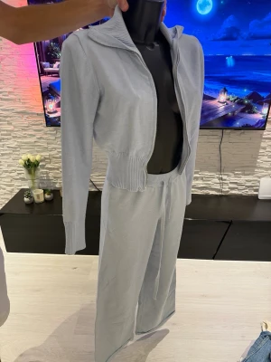 Ljusblått loungewear-set med dragkedja - Mysigt loungewear-set i ljusblått med långärmad ziptröja och matchande byxor med dragsko i midjan. Tröjan har ribbade muddar och hög krage. Materialet ser ut att vara mjukt och stretchigt, perfekt för avslappnade dagar hemma.