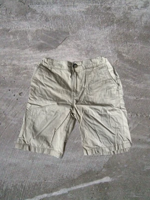 Beige bomullsshorts med fickor - Klassiska beige shorts i bomull med normal passform. Shortsen har två sidofickor fram och två bakfickor, samt knapp och gylf framtill. Perfekta för varma dagar och enkel att matcha med olika stilar.