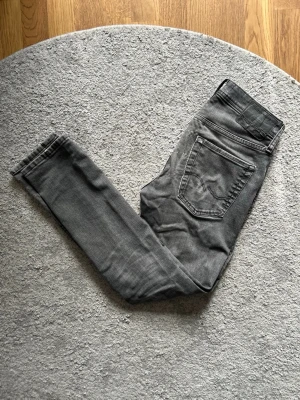 Grå skinny jeans från Jack & Jones - Snygga grå skinny jeans från Jack & Jones med slitningar på ena benet och knappar i gylfen. Jeansen har klassisk femficksmodell och är tillverkade i stretchigt denimtyg för en bekväm passform.