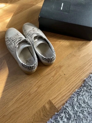 Saint Laurent med leoparddetalj - Snygga vita sneakers med leopardmönstrad detalj på hälen. Klassisk låg modell med vita snören och gummisula. Perfekta för dig som vill ha en clean look med en twist. Passar 41 