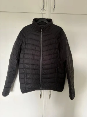 Svart dunjacka från TwentyFour  - Säljer en svart pufferjacka med hög krage och hel dragkedja framtill. Jackan har två sidofickor med dragkedja och quiltad design. Perfekt för kalla dagar och riktigt skön att bära. Materialet ser ut att vara syntetiskt och jackan har en stilren look. 