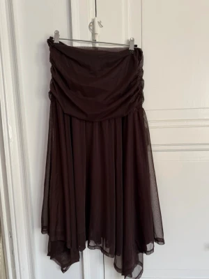 Saemdi studios - Brun långkjol med draperad midja - Säljer en brun långkjol med draperad midja och asymmetrisk nederkant. Kjolen har ett tunt, flygigt tyg som ger ett snyggt fall och passar perfekt till olika stilar. Enkel att matcha med både toppar och stickade tröjor.