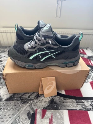 Asics GEL-NYC RGD grå/grön sneakers - Snygga Asics GEL-NYC RGD sneakers i grafitgrått med detaljer i mintgrönt och svart. Ovandelen är i mesh och syntetmaterial för bra andningsförmåga och komfort. Klassisk Asics-logga på sidan och GEL-dämpning i sulan för extra skön känsla. Använda endast 3 gånger.