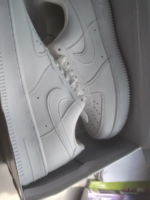 Helvita låga sneakers - Säljer ett par helvita sneakers med klassisk siluett och perforerade detaljer på tån. Skorna har låga kanter, vita skosnören och en tjock sula. Materialet ser ut att vara slätt läder eller konstläder. Perfekta för en clean och stilren look.