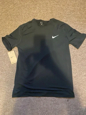Svart Nike sport t-shirt - Svart sport t-shirt  med klassisk vit logga på bröstet. Tillverkad i ett lätt och snabbtorkande material som passar perfekt för träning. T-shirten har rund halsringning och korta ärmar. En stilren och funktionell tränings-tisha.