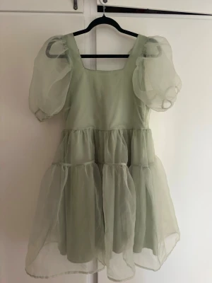 Ljusgrön puffärm klänning - Supersöt ljusgrön klänning med puffärmar och volangkjol. Klänningen har fyrkantig ringning, smock i ryggen och är gjord i ett tunt, skirt material som ger ett drömmigt intryck. Perfekt för dig som gillar romantisk och trendig stil.