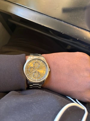 Stilren silverfärgad klocka - Snygg och modern klocka i silverfärg med metallarmband och rund urtavla. Klockan har flera små urtavlor för dag, datum och 24-timmarsvisning. Enkel och stilren design som passar till det mesta.