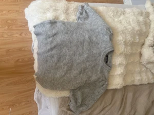 Ljusgrå stickad tröja - Mysig ljusgrå stickad tröja med rund hals och långa ärmar. Tröjan har en enkel och klassisk design som passar perfekt till lager på lager. Materialet ser mjukt och fluffigt ut, vilket gör den extra bekväm.