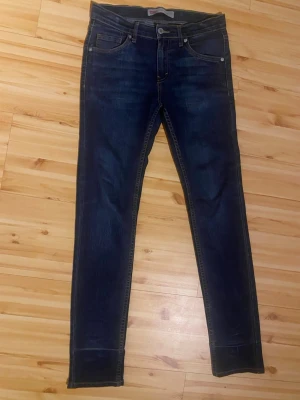Mörkblå skinny jeans med stretch - Snygga mörkblå skinny jeans med klassisk femficksdesign och smal passform. Jeansen har diskreta slitningar och kontrastsömmar. Tillverkade i stretchigt denimtyg för extra komfort och rörelsefrihet. Perfekta till en avslappnad och trendig look.
