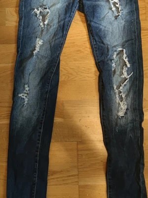 Snygga slitna Zara TRF jeans strl 36 - Säljer ett par supersnygga, mörkblå jeans från Zara TRF (Premium Wash) i storlek 36. Modellen har en jättefin tvätt med fabriksgjorda slitningar och hål längs benen som ger en cool streetwear-look. Skön passform med lite stretch!