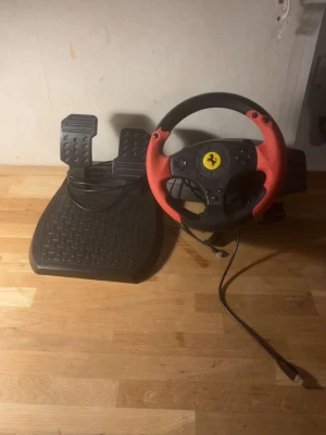 Ratt och pedaler till spelkonsol - Säljer en gamingratt med tillhörande pedaler, perfekt för racing- och bilspel. Ratten är svart med röda detaljer och har en klassisk sportbilsdesign. Pedalerna är svarta och har halkskyddad yta. Ansluts via USB-kabel.