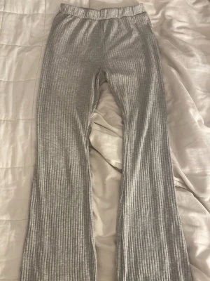 Grå ribbade mjukisbyxor (tall)  - Säljer ett par grå mjukisbyxor med ribbad struktur och utsvängda ben. Byxorna har resår i midjan och är gjorda i ett mjukt, stretchigt material som känns skönt mot huden. Perfekta för en avslappnad och chill stil.