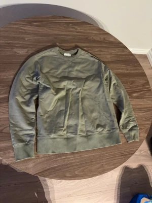 Olivgrön sweatshirt med rund hals - En stilren olivgrön sweatshirt med rund halsringning och ribbade muddar vid ärmslut och nederkant. Tröjan har en avslappnad passform och är tillverkad i mjukt material, perfekt för en casual look.