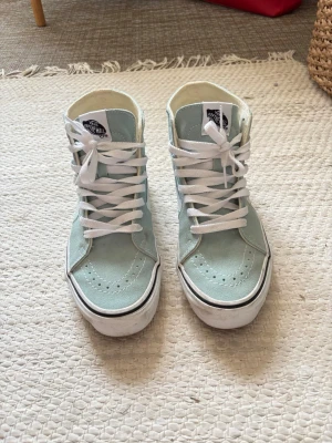 Mintgröna Vans Sk8-Hi sneakers - Säljer ett par mintgröna Vans Sk8-Hi sneakers med vit sula och klassisk vit sidostripes. Skorna har högt skaft, vita skosnören och är tillverkade i canvas med detaljer i mocka. Perfekta för dig som vill ha en stilren och fräsch look.