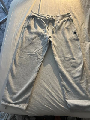 Grå mjukisbyxor från Polo Ralph Lauren - Snygga grå mjukisbyxor från Polo Ralph Lauren med dragsko i midjan och två sidofickor. Byxorna har en avslappnad passform och är tillverkade i mjukt sweatshirtmaterial. Klassisk logga broderad på vänster ficka.