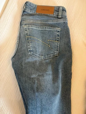 Blå bootcut jeans från Junkyard - Snygga blå jeans från Junkyard med klassisk femficksmodell och utsvängda ben. Jeansen har en ljus tvätt och cool detalj med kontrastsömmar på bakfickan. Perfekta till vardagslooken och passar till det mesta. Materialet är mjukt denim i bomull.