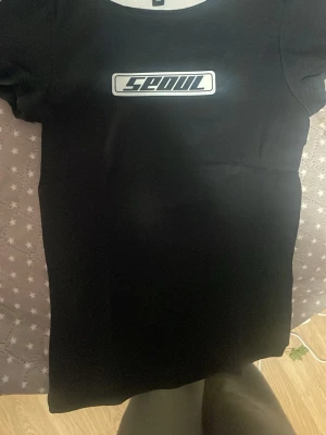 Svart t-shirt med Seoul-tryck Divided - Cool svart t-shirt från Divided med ett vitt tryck där det står 'Seoul' på bröstet. Klassisk passform och korta ärmar, perfekt till jeans eller kjol. Enkel och stilren design som funkar till många olika looks.