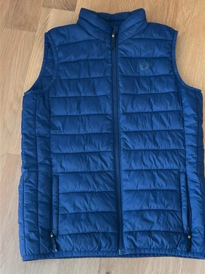 Marinblå dunväst från Hangten - Snygg marinblå dunväst från Hangten med ståkrage och dragkedja framtill. Västen har två fickor med dragkedja och quiltad design. Perfekt för lager på lager och ger en sportig look.