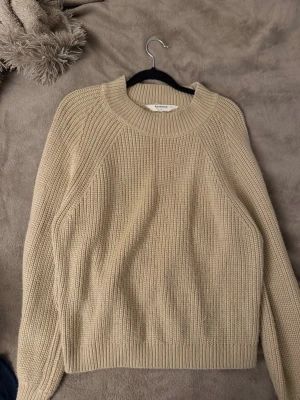 Beige stickad tröja  - En stilren beige stickad tröja med rund halsringning och ribbade muddar. Tröjan har en klassisk rak passform och är perfekt för svala sommarkvällar eller höstliga dagar. Materialet är mjukt och ger en mysig känsla. Passar även XS/S