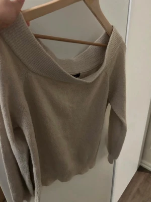 Beige stickad tröja Gina Tricot - Mysig beige stickad tröja från Gina Tricot med bred ribbad krage och långa ärmar. Tröjan har en avslappnad passform och är perfekt för kalla dagar. Materialet är mjukt och bekvämt, vilket gör den skön att bära hela vintern.